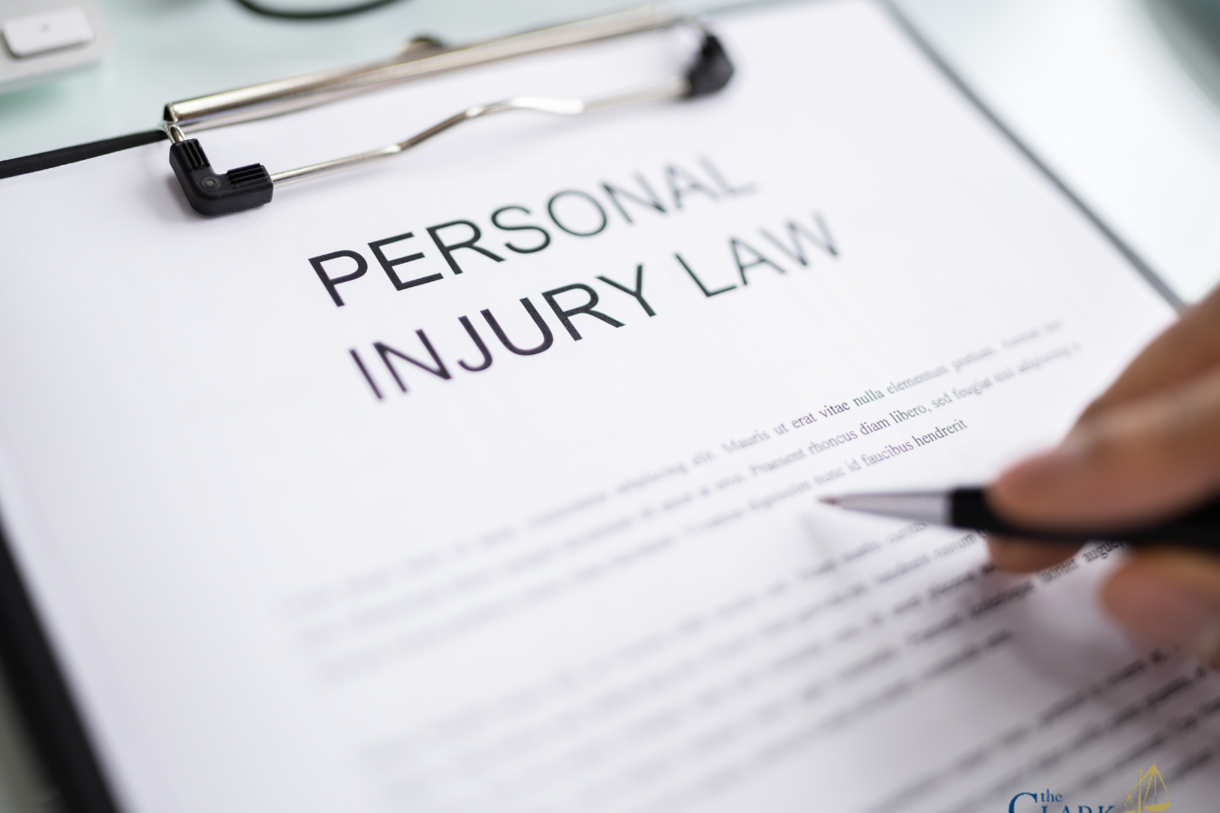 A clipboard holds a document titled "Personal Injury Law" with a hand holding a pen hovering over the paper; The Clark Law Office logo appears in the bottom right corner.
