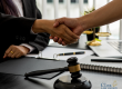 Two people shaking hands across a desk with legal documents, a gavel, and office supplies visible; Clark Law Office logo in the corner.