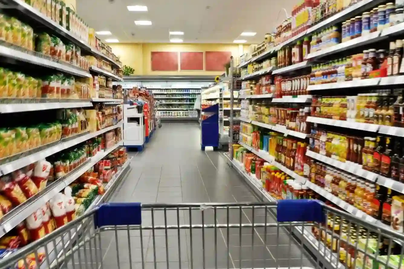 A shopping cart is pushed down an aisle in a well-lit supermarket, with shelves stocked with various packaged food items on both sides. A shopping cart is pushed down an aisle in a well-lit supermarket, with shelves stocked with various packaged food items on both sides.