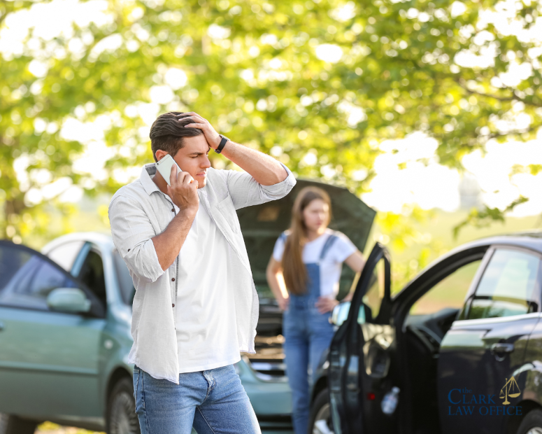A man stands by two cars with damage, talking on his phone and looking stressed, while a woman stands near one open car door with a raised hood. A man stands by two cars with damage, talking on his phone and looking stressed, while a woman stands near one open car door with a raised hood.