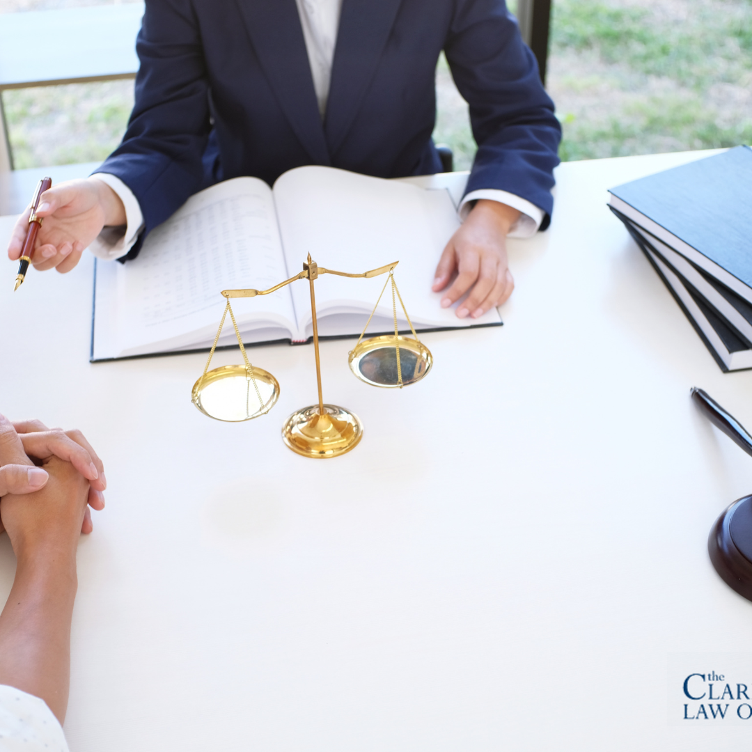 Two people sit across from a lawyer at a desk with legal books, scales of justice, and a gavel. The Clark Law Office logo is visible in the corner. Two people sit across from a lawyer at a desk with legal books, scales of justice, and a gavel. The Clark Law Office logo is visible in the corner.