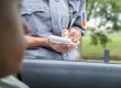 A police officer in uniform writes a ticket while standing outside a car window, with part of the driver’s face visible in the foreground.