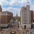 A street view in downtown Lansing, Michigan, with the Michigan State Capitol building in the background and an American flag atop a tall building.