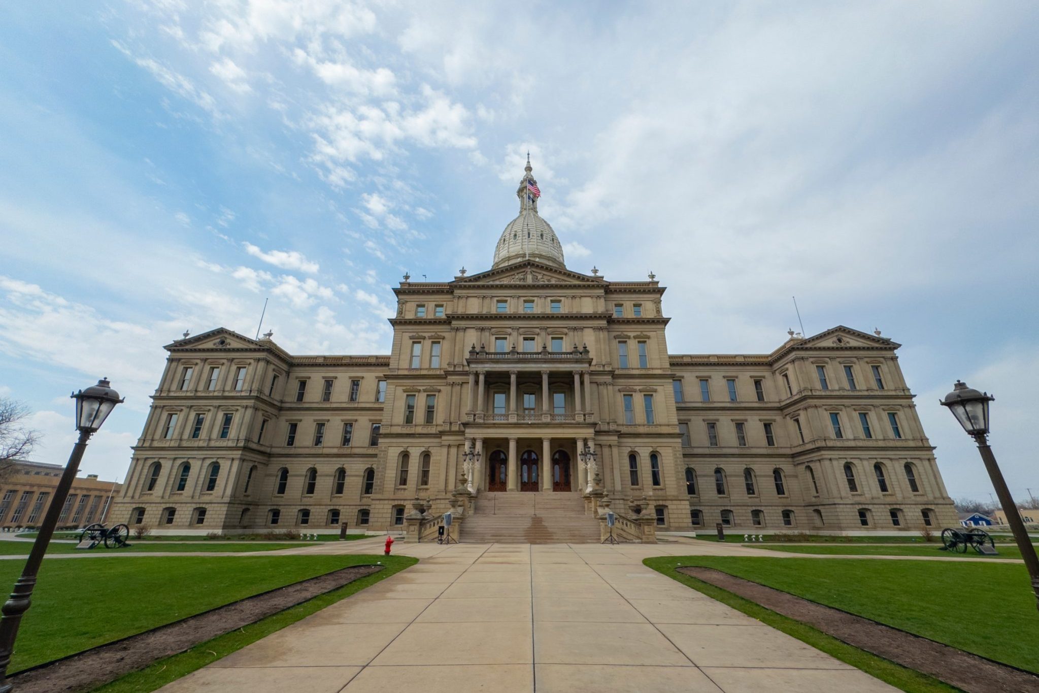 What Happens If a State Employee Is Injured on the Job in Lansing A wide-angle view of the Michigan State Capitol building with a central dome, symmetrical wings, and cloudy sky above.