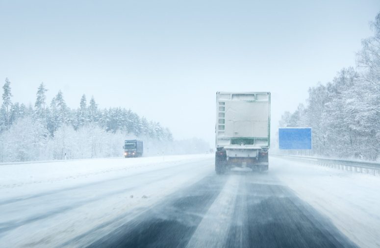 When Black Ice Is Not a Legal Defense for Truck Drivers in Michigan A truck drives on a snow-covered highway with trees lining the road and another vehicle approaching from the opposite direction in wintry conditions.