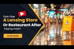 A wet floor caution sign stands in a brightly lit store aisle; text asks about suing a Lansing store or restaurant after slipping inside.