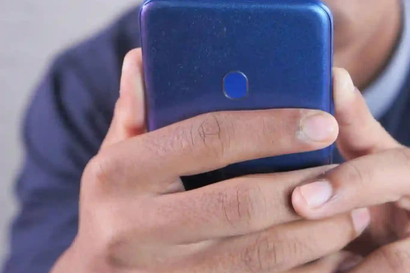 A person wearing glasses holds and looks at a blue smartphone, with their face partially visible in the background.