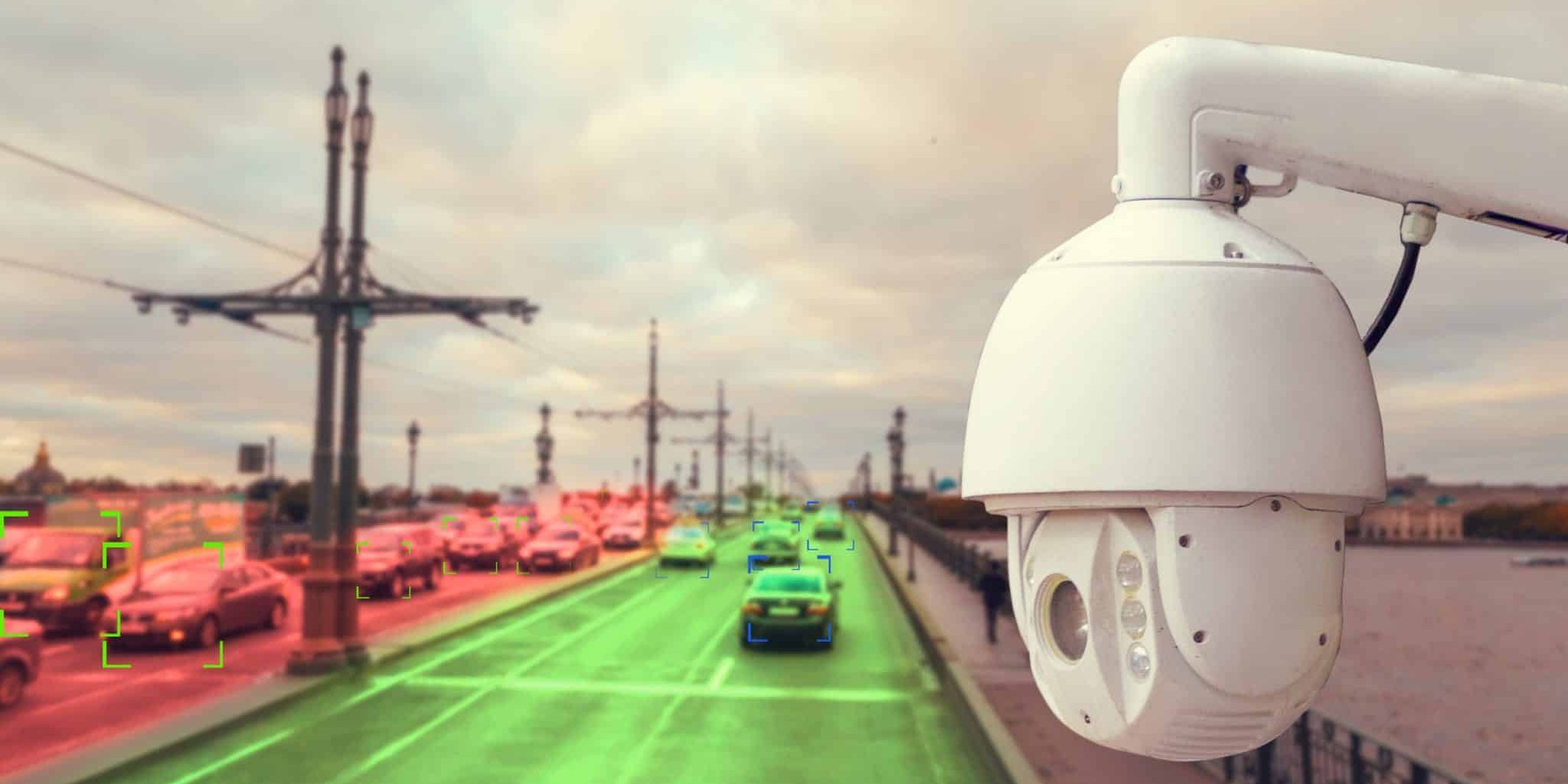 Flock cameras, ai, and marijuana Surveillance camera overlooking a busy city bridge with cars; some vehicles highlighted in green and red, suggesting automated traffic monitoring.
